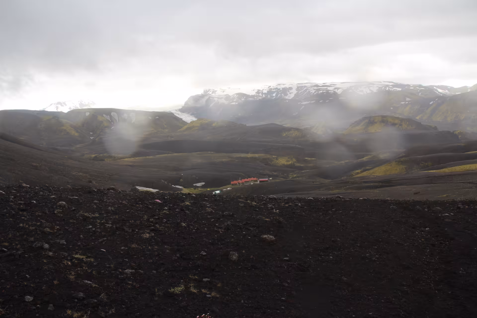 Black volcanic landscape with red-roofed hut in misty valley near Thorsmork glacier Iceland