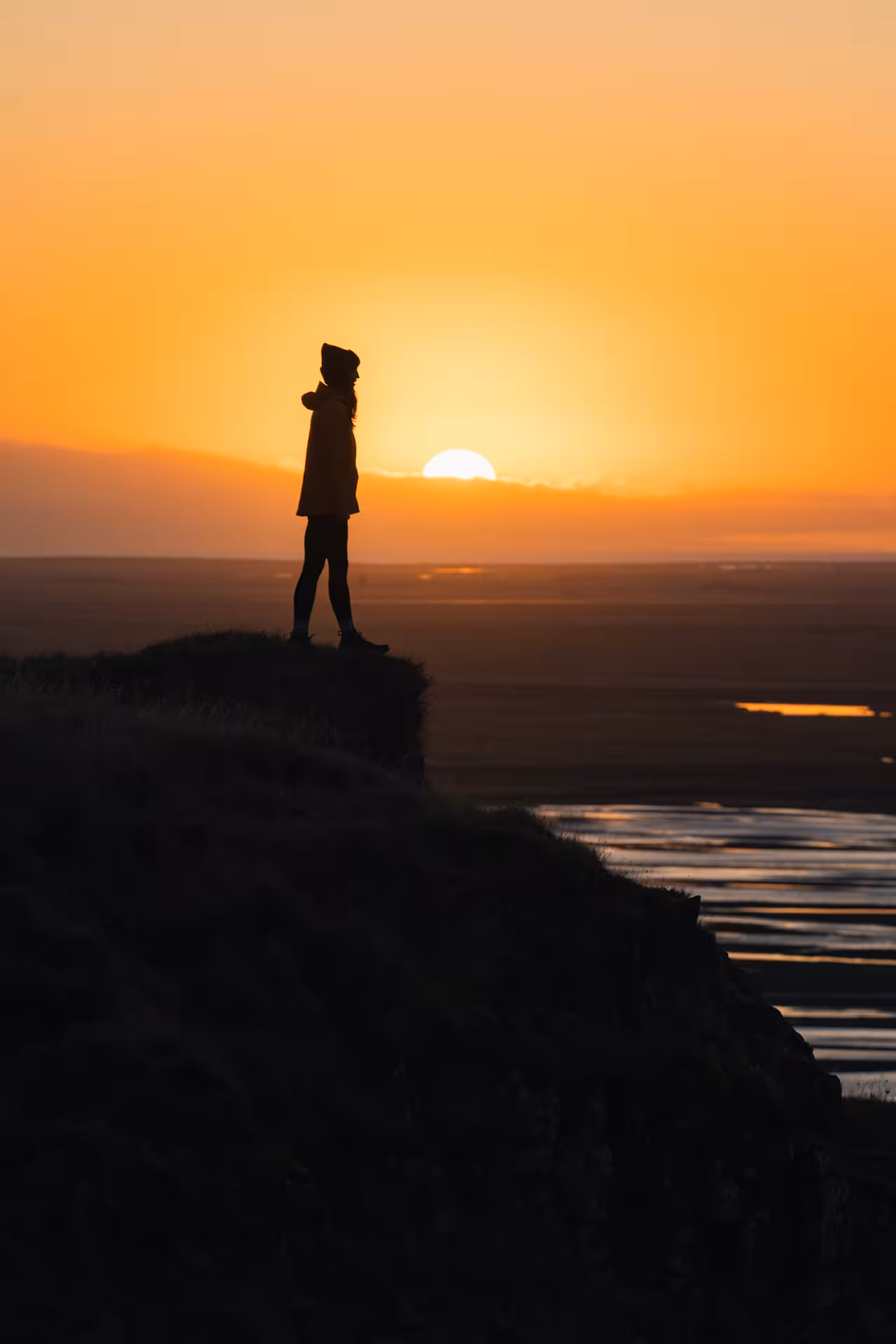 Silhouette of person standing on highland cliff overlooking Icelandic landscape at golden sunset