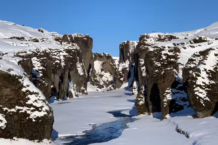 Snow-covered Fjaðrárgljúfur canyon with frozen river and towering basalt rock walls in winter Iceland