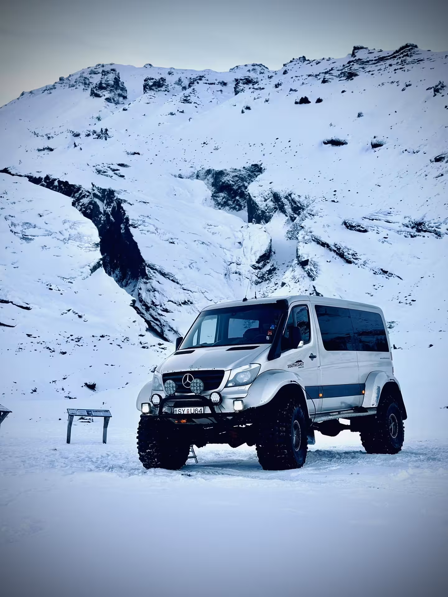 Modified Mercedes Sprinter super jeep with large off-road tires parked on snow in front of Icelandic mountains