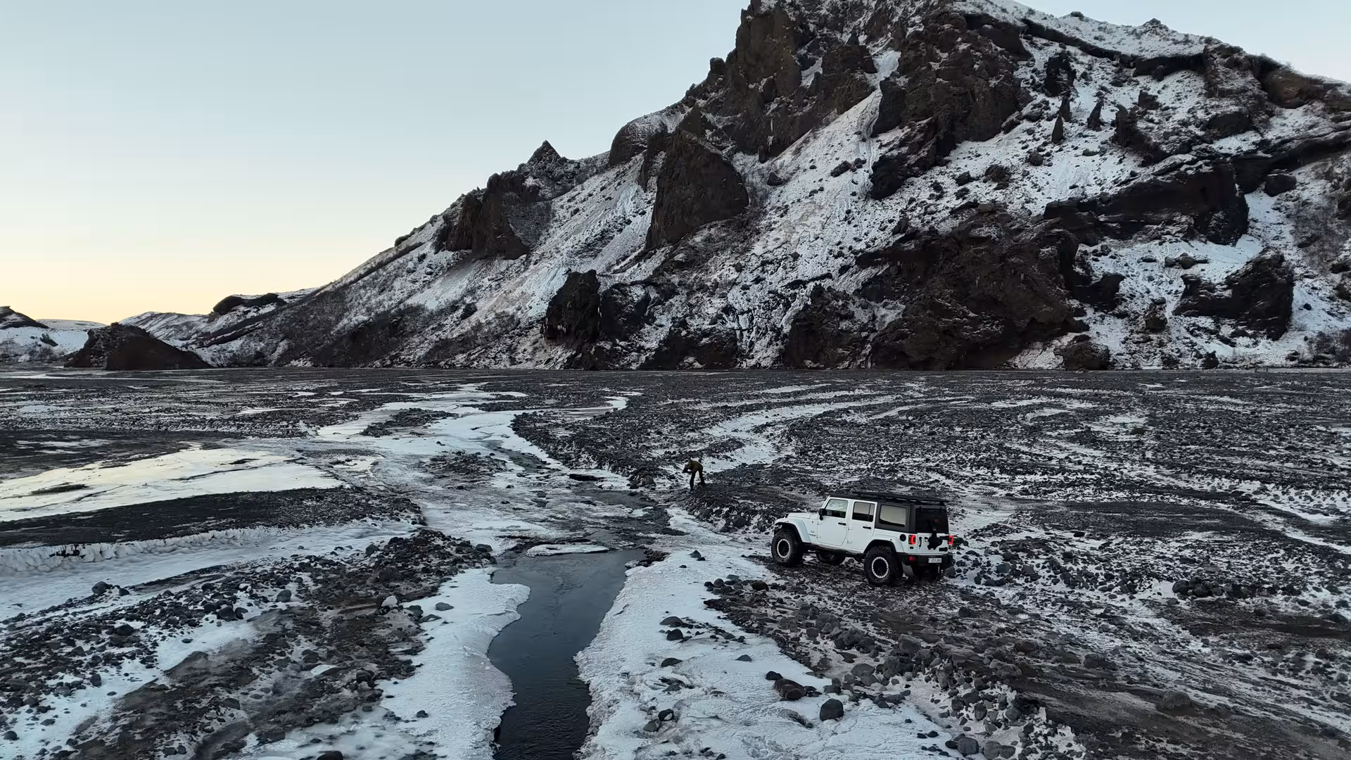 White Super Jeep on snowy black volcanic terrain in Thorsmork Iceland Highlands with dramatic rocky mountain backdrop