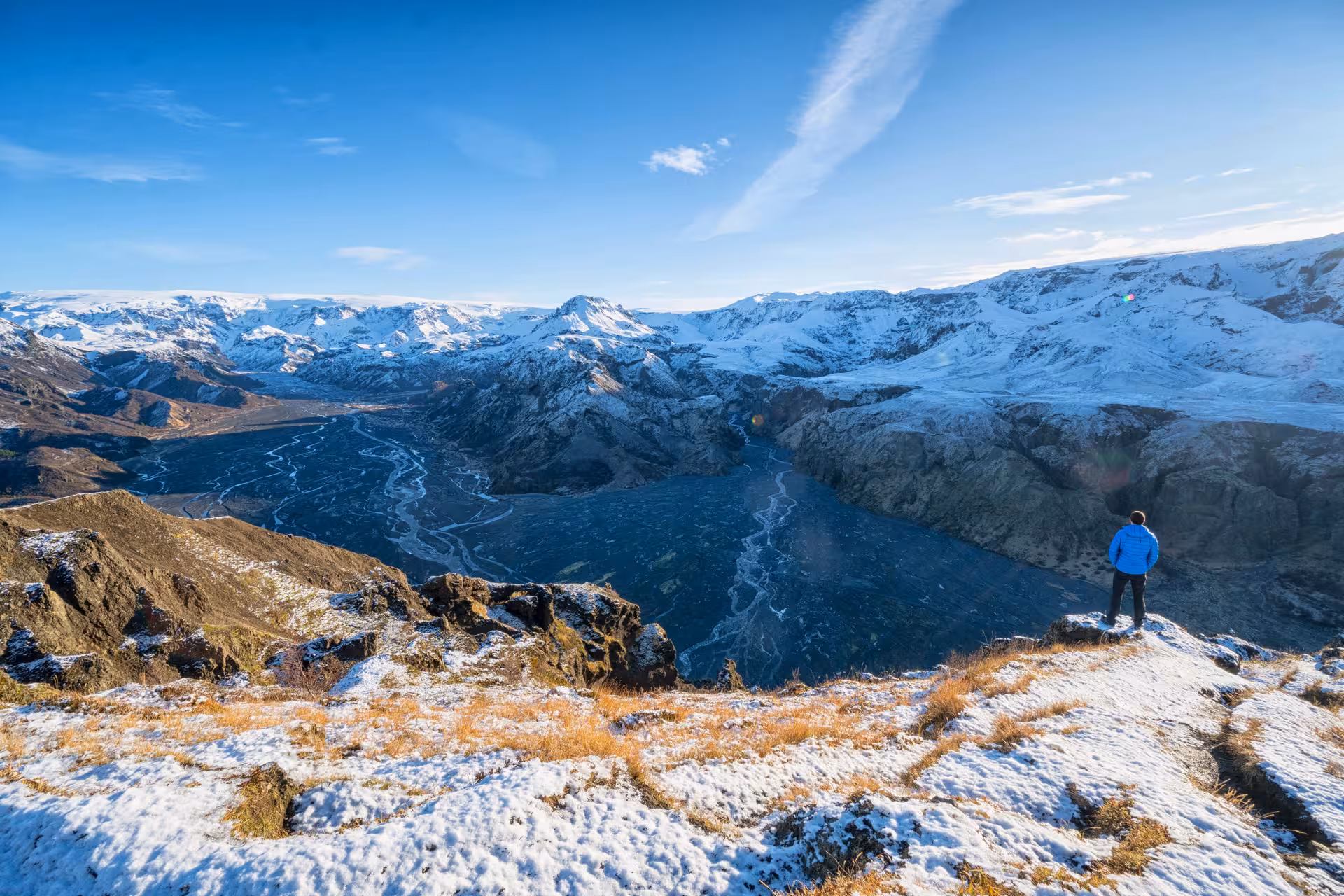 Hiker in blue jacket overlooking Thorsmork valley with braided glacial rivers and snow-capped mountains in Iceland