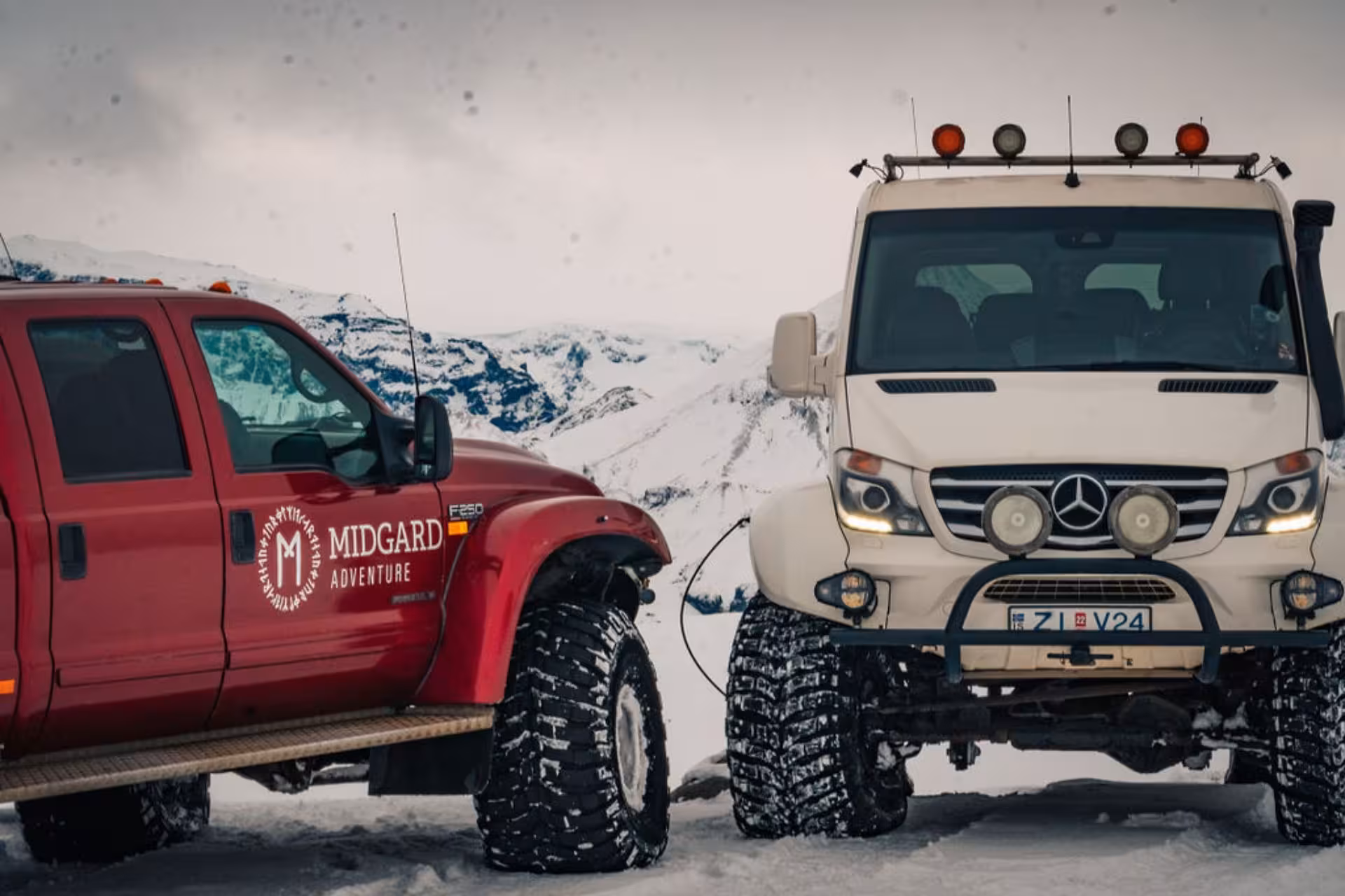 Two large off-road super jeeps parked on a snowy highland with volcanic mountains in the background
