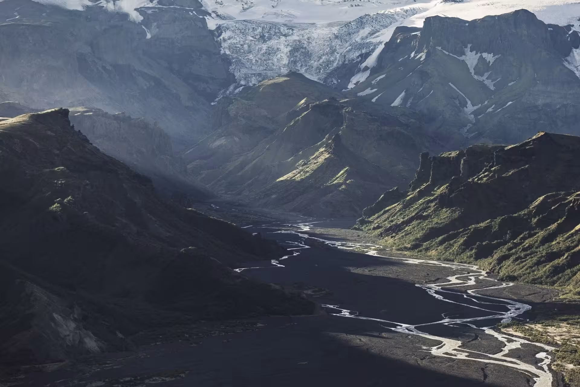 Aerial view of Thorsmork valley with braided glacial river, black sand plains, and snow-capped mountains in Iceland