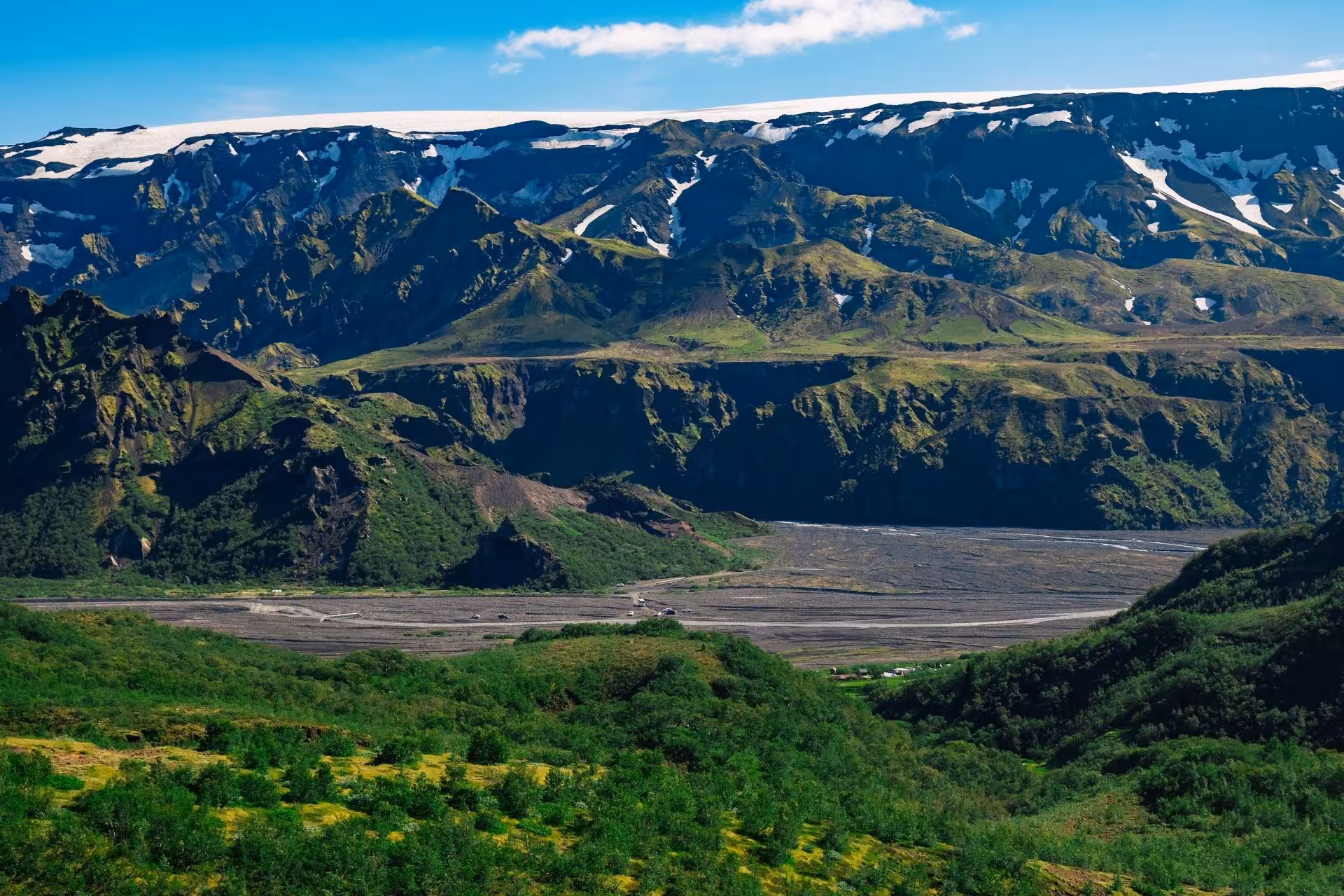 Panoramic view of Thorsmork valley with green slopes, black sand river plain, and glacier-capped mountains in Iceland
