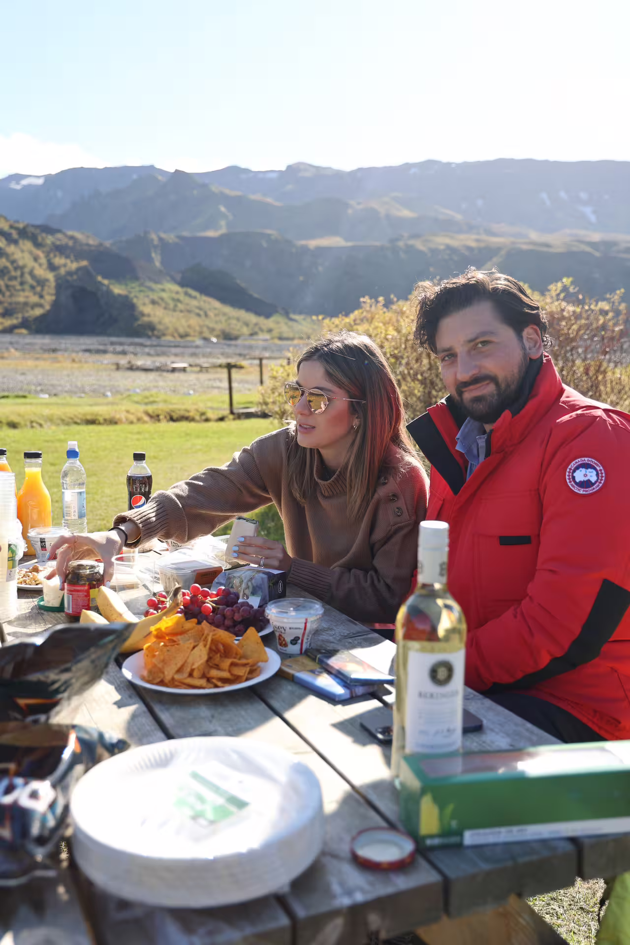 Couple enjoying outdoor picnic lunch with snacks and wine overlooking Thorsmork mountain valley on Iceland 4x4 tour