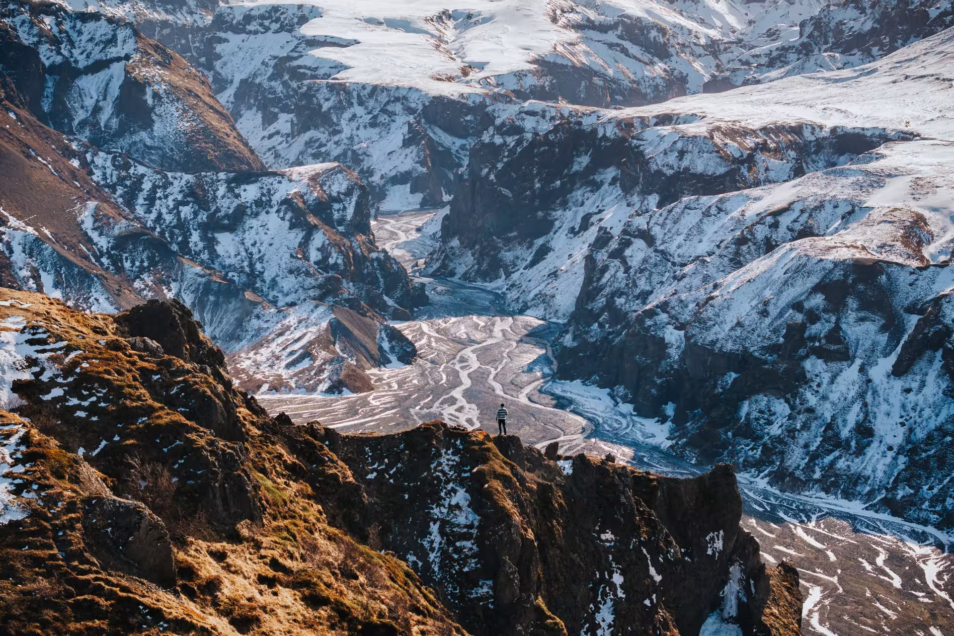 Hiker standing on rocky cliff overlooking Thorsmork valley with braided glacier rivers and snow-capped mountains in Iceland