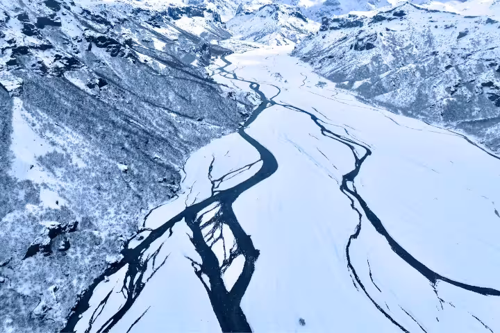 Aerial view of snow-covered Thorsmork valley with winding dark river channels between icy mountains in Iceland