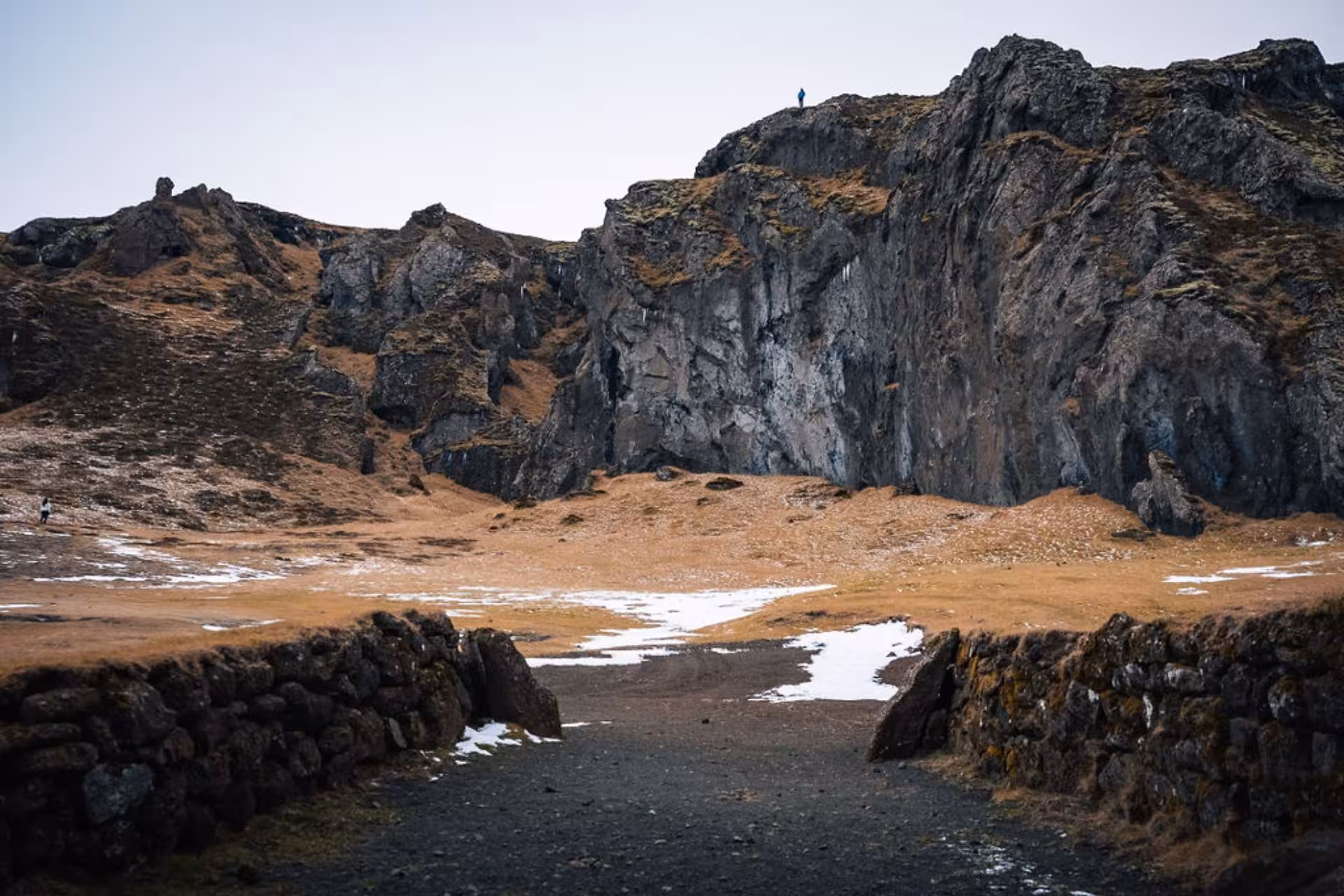 Rocky volcanic cliffs and snow-dusted highlands in Thorsmork with a lone hiker on the summit