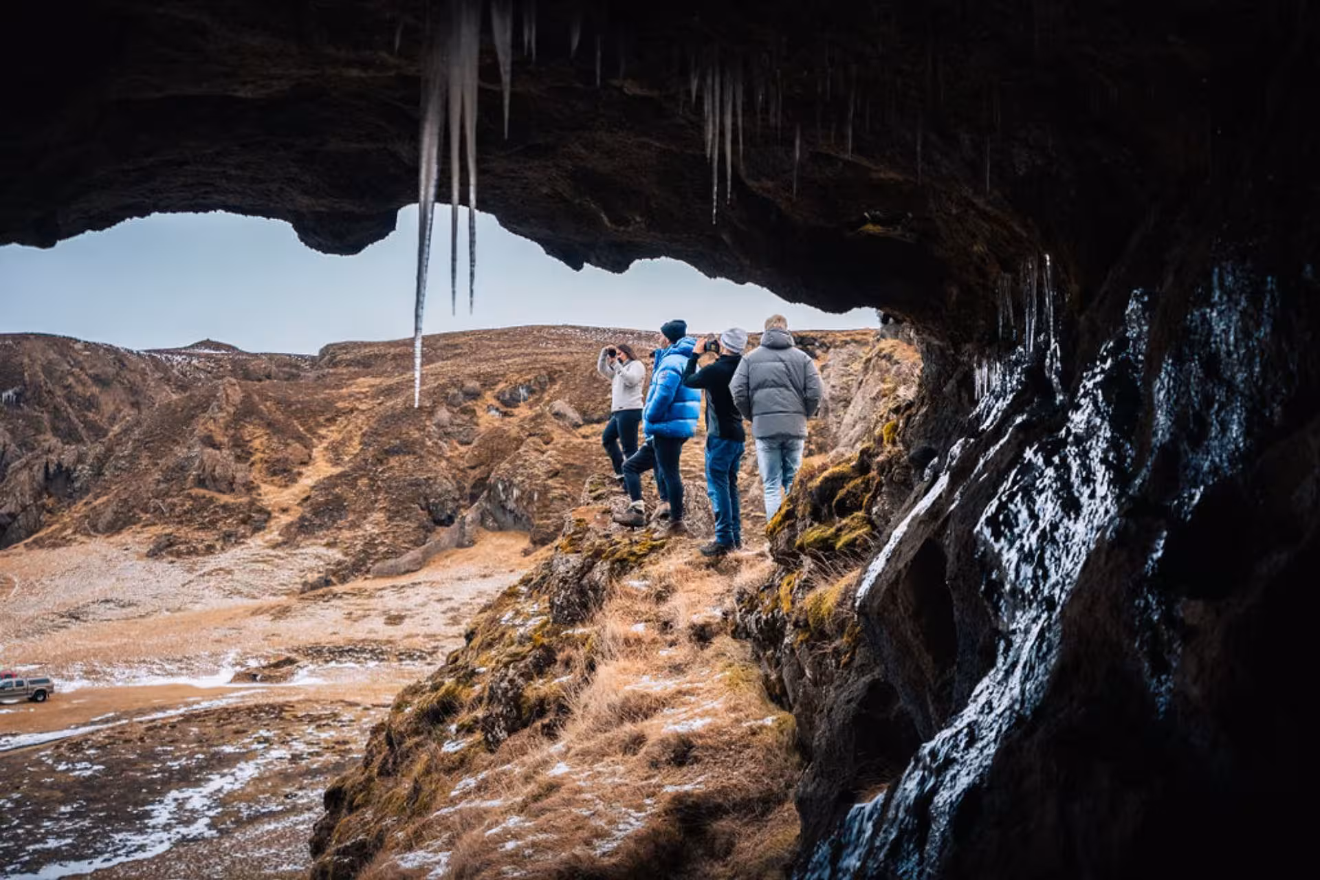 Tourists photographing volcanic highland landscape from inside an icy cave in Thorsmork, Iceland