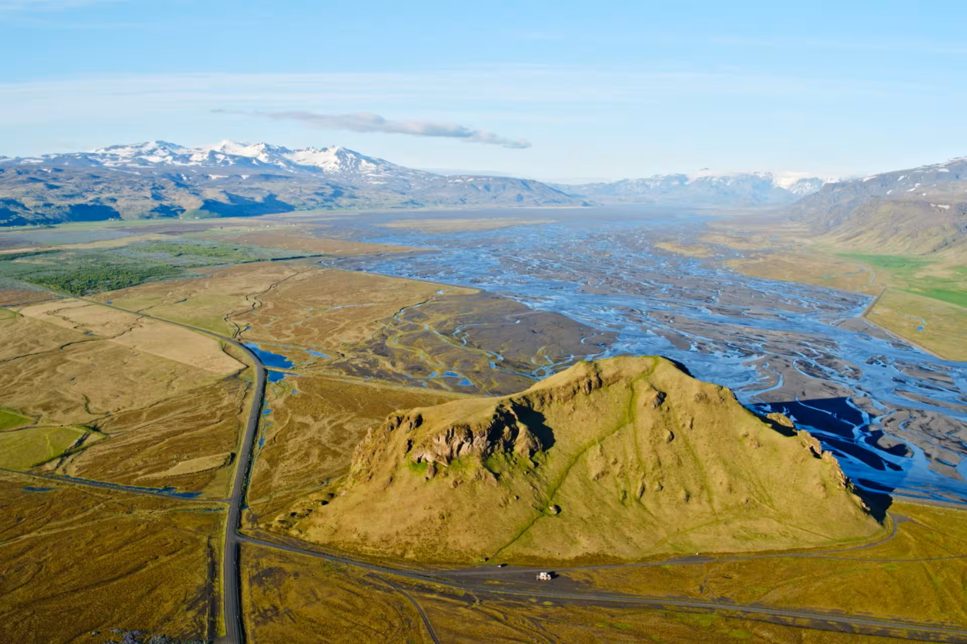 Aerial view of Thorsmork volcanic highlands with braided glacial rivers, green hill, and snow-capped mountains in Iceland