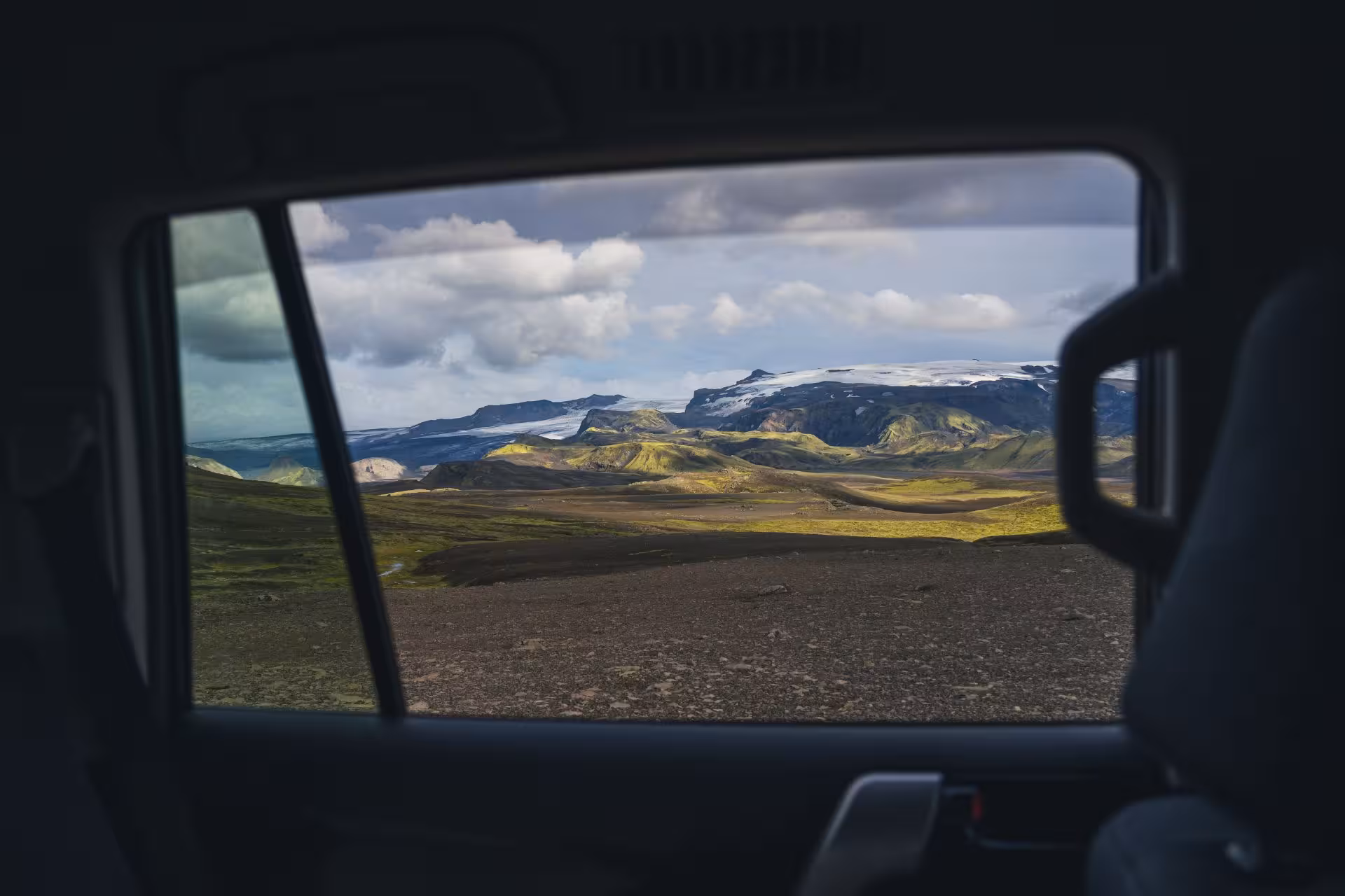 View through car window of Thorsmork volcanic highlands with glacier-capped mountains and green moss-covered terrain