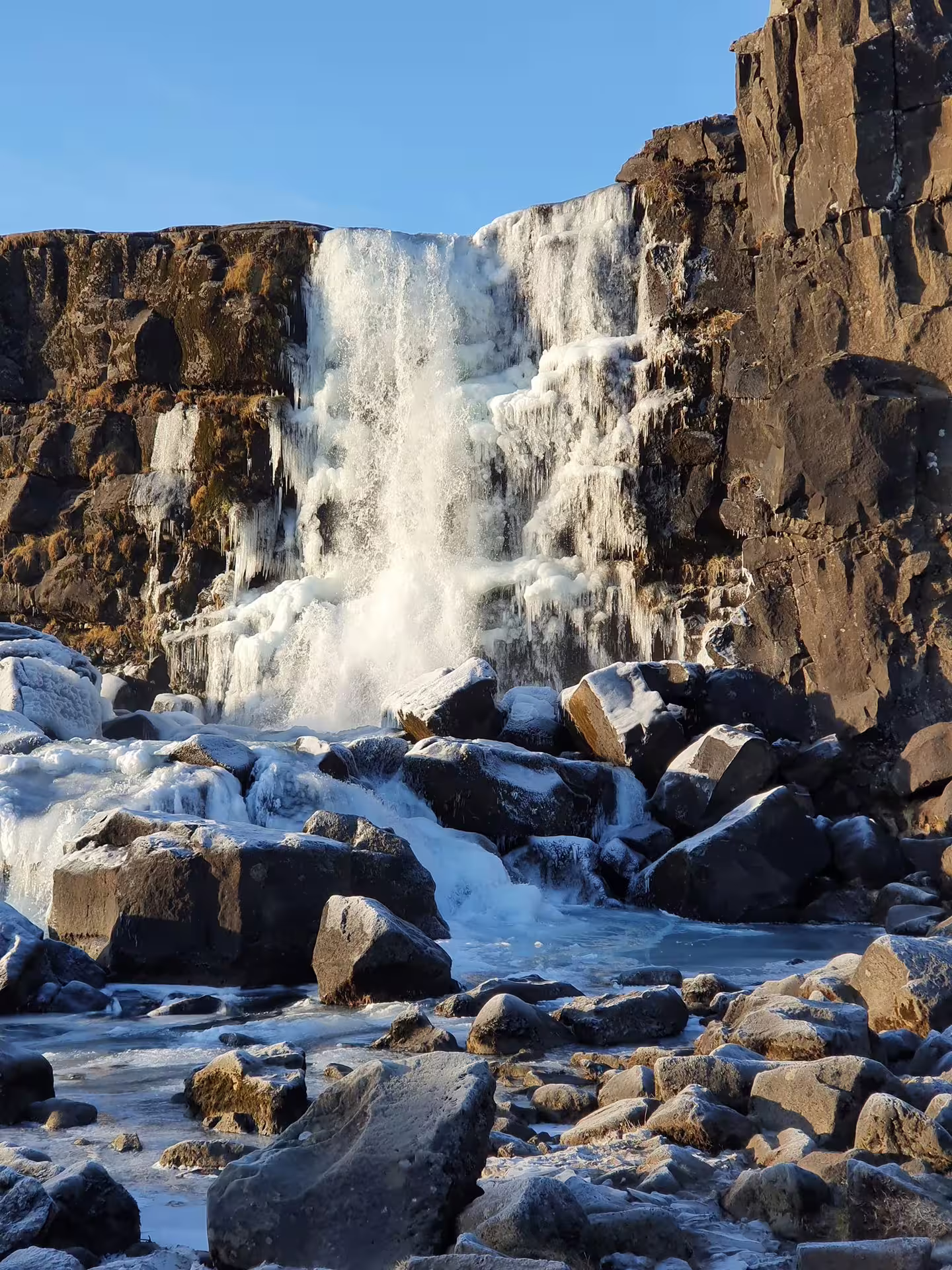 Partially frozen Öxará waterfall cascading over dark basalt rocks in winter, Þingvellir Iceland