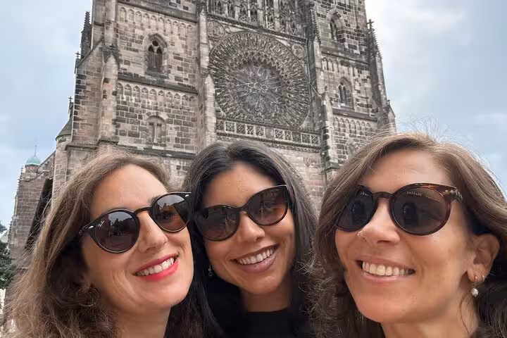 Three women smiling in front of St. Lawrence Church during a Nuremberg walking tour