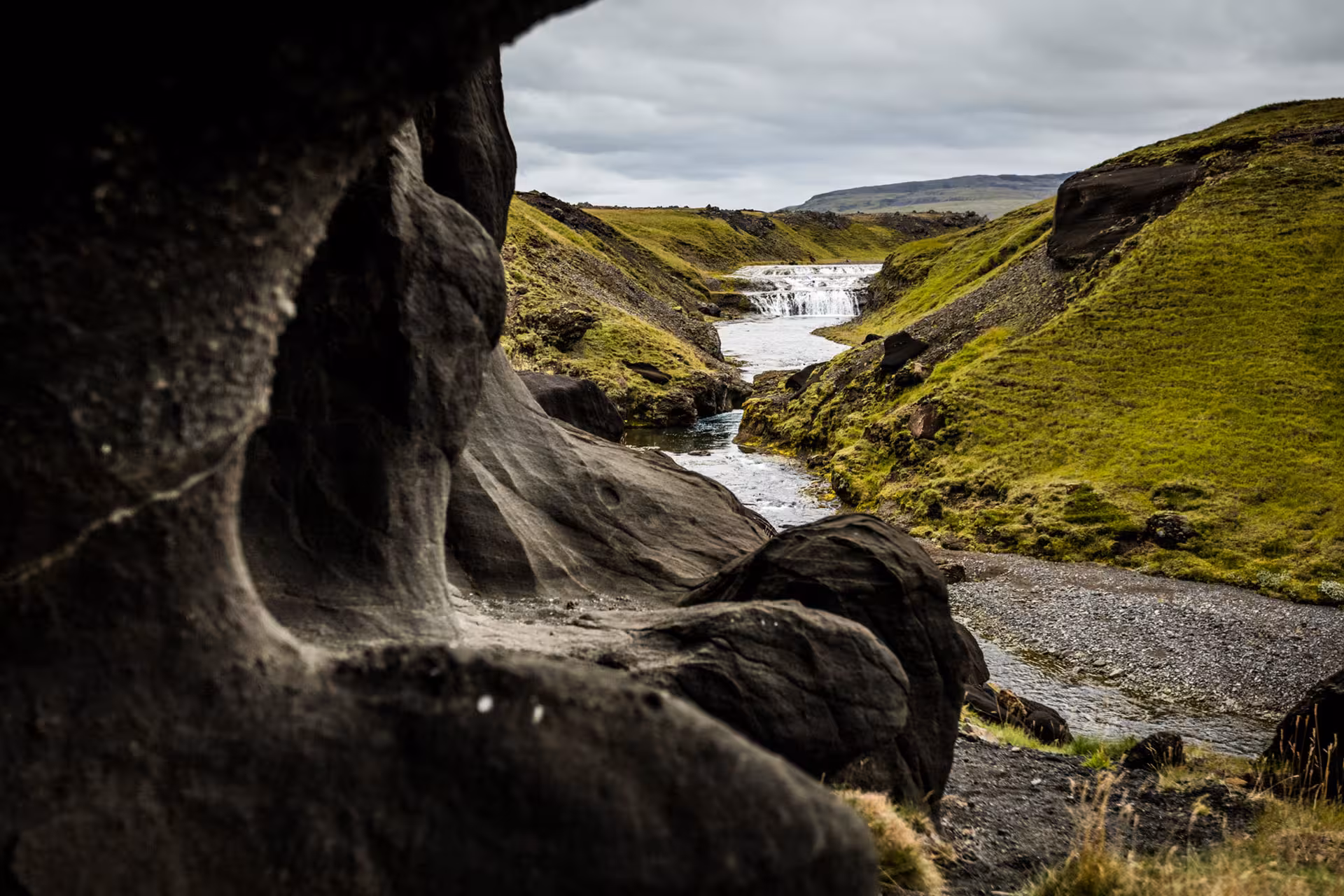 Rocky canyon with flowing river and waterfall framed by green moss-covered hills in South Iceland
