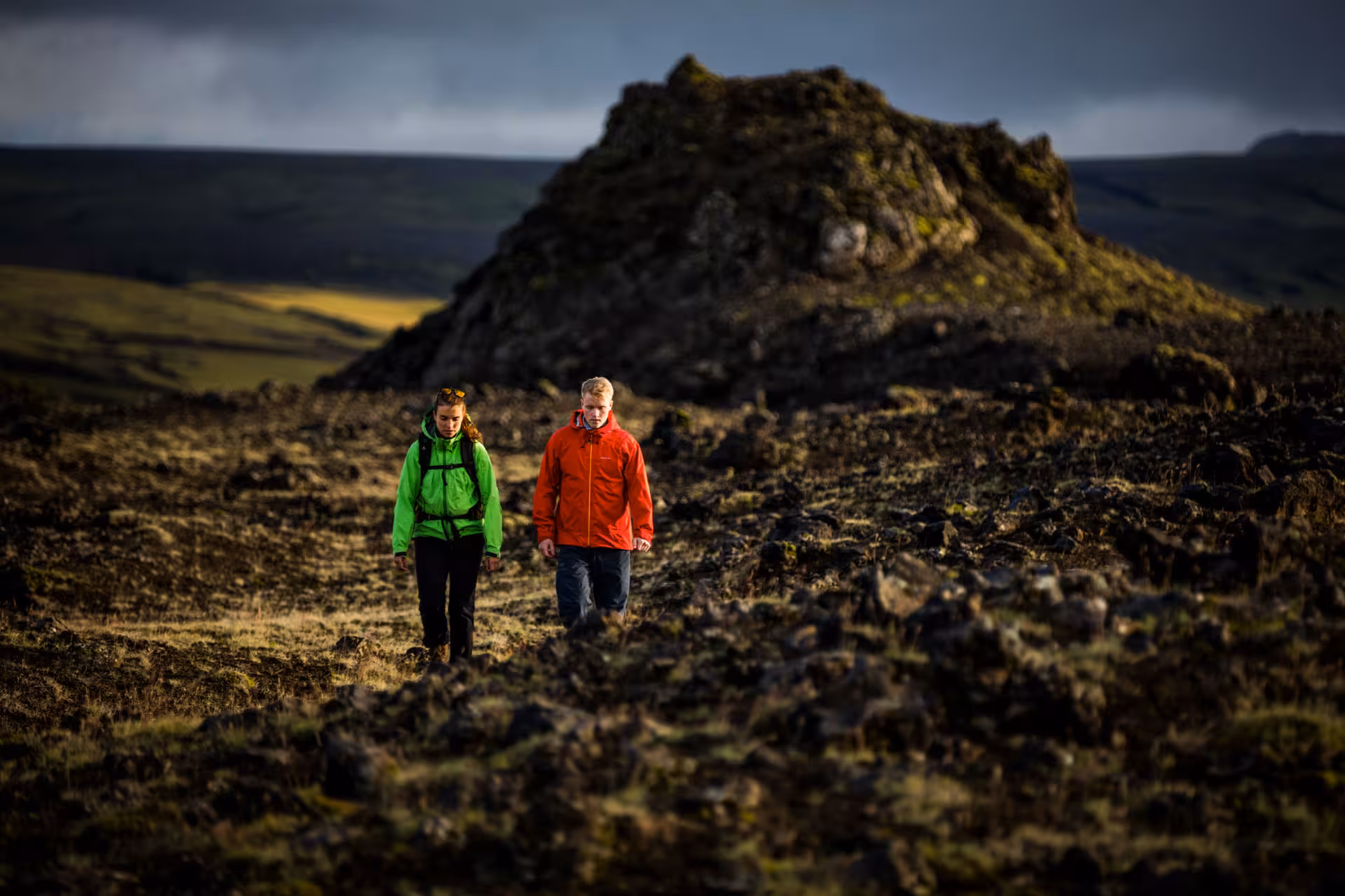 Two hikers in green and red jackets trekking rocky volcanic landscape in South Iceland