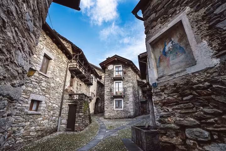 Charming cobblestone street in a historic Ticino village, lined with rustic stone houses and quaint balconies.