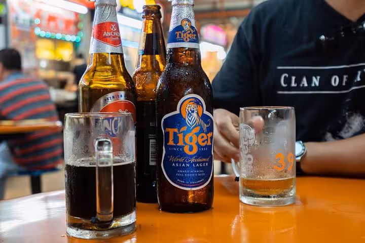 Close-up of Tiger beer bottles and glasses on a table at a lively Singapore street food market.