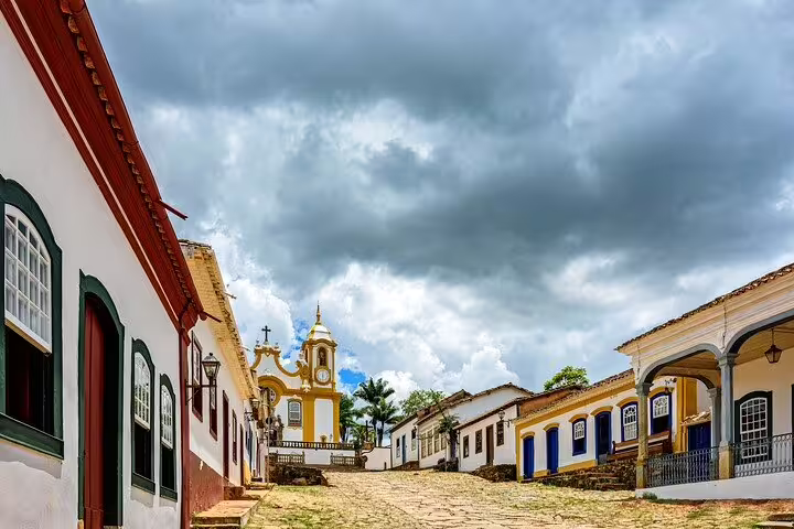 Charming colonial street in Tiradentes with colorful buildings and a historic church under dramatic skies.
