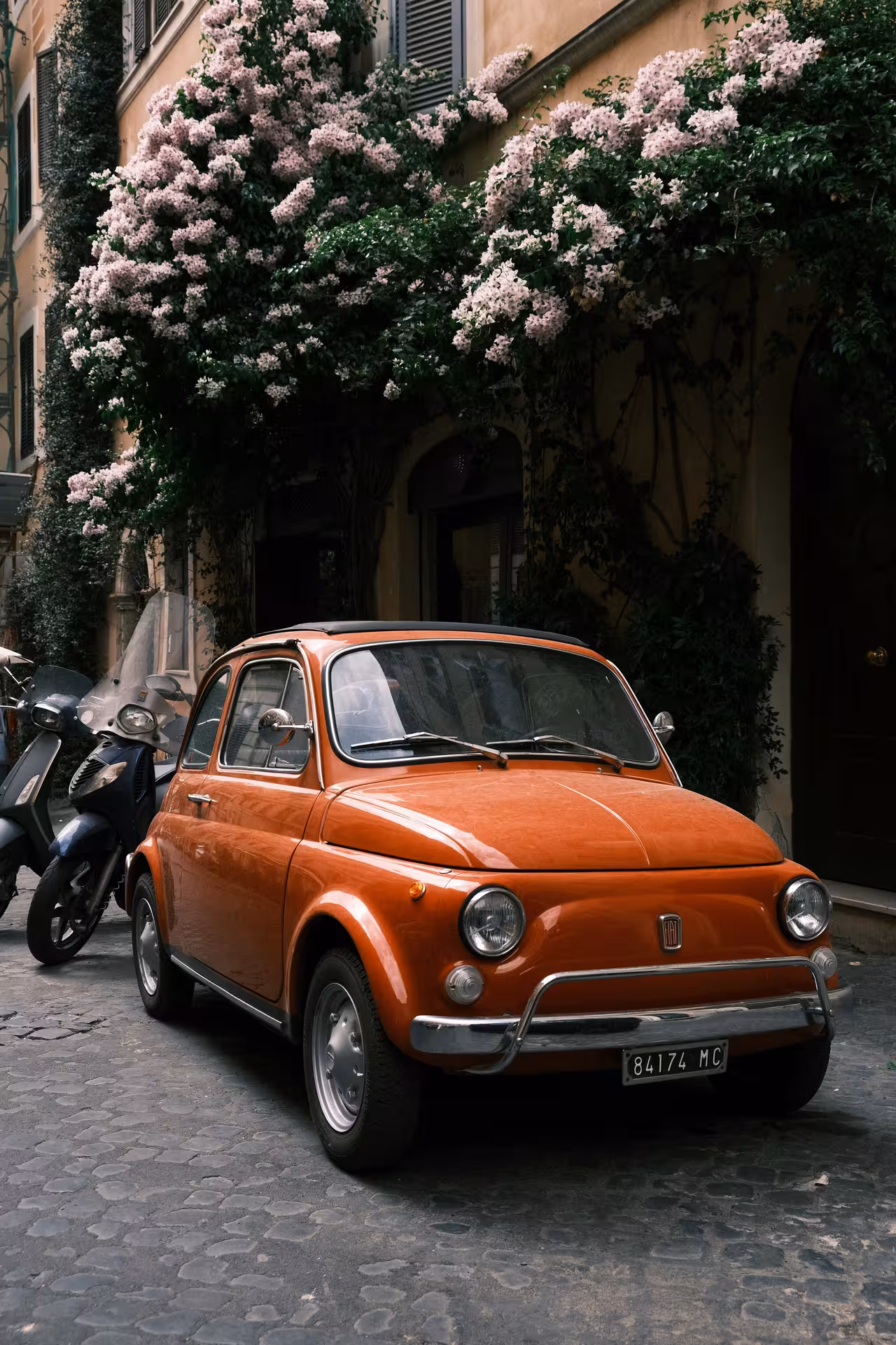 Iconic orange Fiat 500 parked under blooming flowers, a highlight of Tivoli Vintage Tour by Fiat 500.