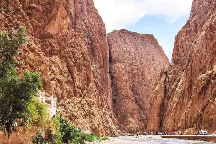 Stunning view of Todra Gorge's towering red cliffs and a scenic road on the Morocco desert tour from Fes to Marrakech.