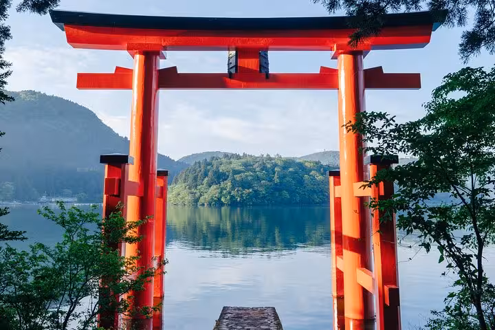 Vibrant red torii gate framing a serene view of Lake Ashi surrounded by lush greenery in Hakone.