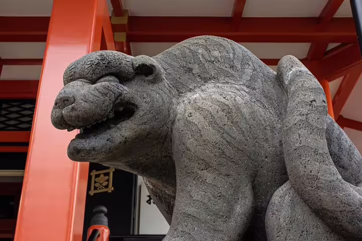 Stone guardian lion-dog statue at a Tokyo shrine with red torii gate structure behind