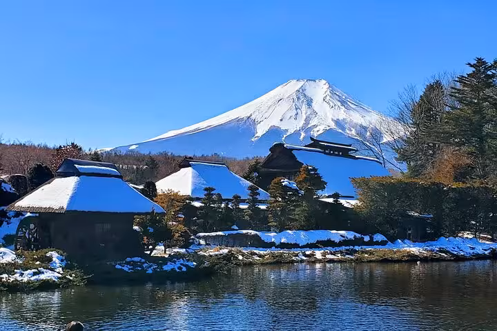 Traditional Japanese village with snow-capped roofs and Mount Fuji in the background, reflecting in a serene pond.