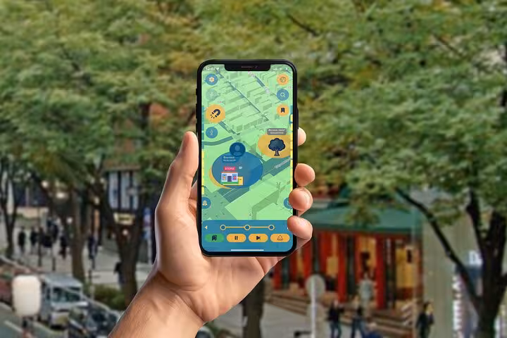 Hand holding a self-guided tour app displaying a map near a lush Tokyo tree-lined street toward Shibuya