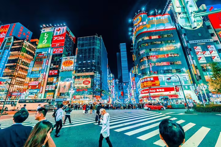 Crowded neon-lit streets of Shinjuku, Tokyo at night with colorful Japanese billboards and pedestrians
