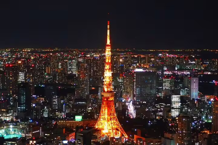 Tokyo Tower illuminated in orange at night surrounded by city lights