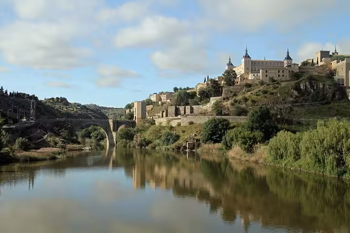 Scenic view of Toledo's Alcázar and ancient bridge reflected in the Tajo River, ideal for a half-day tour from Madrid.