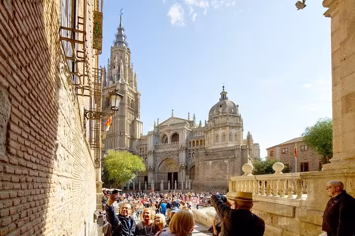 Tourists capturing memories in front of the majestic Toledo Cathedral on a sunny day during a day trip from Madrid.