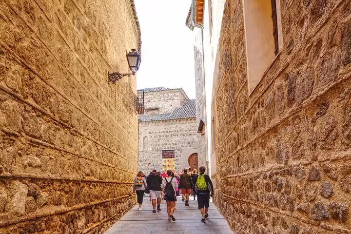Visitors stroll through narrow, ancient stone alleyways in Toledo's historic center during a day tour.