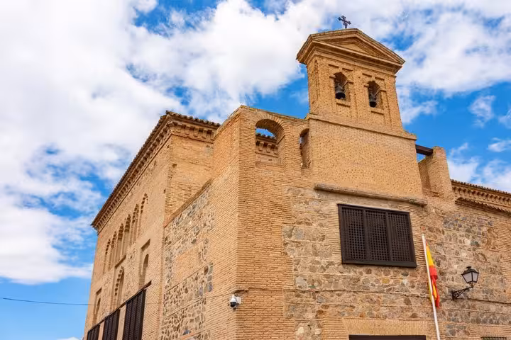 Historic stone church with bell tower and cross in Toledo, Spain, under a blue sky
