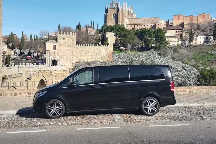 Black minivan parked with Toledo skyline and cathedral behind, ideal for a private half-day tour by minivan