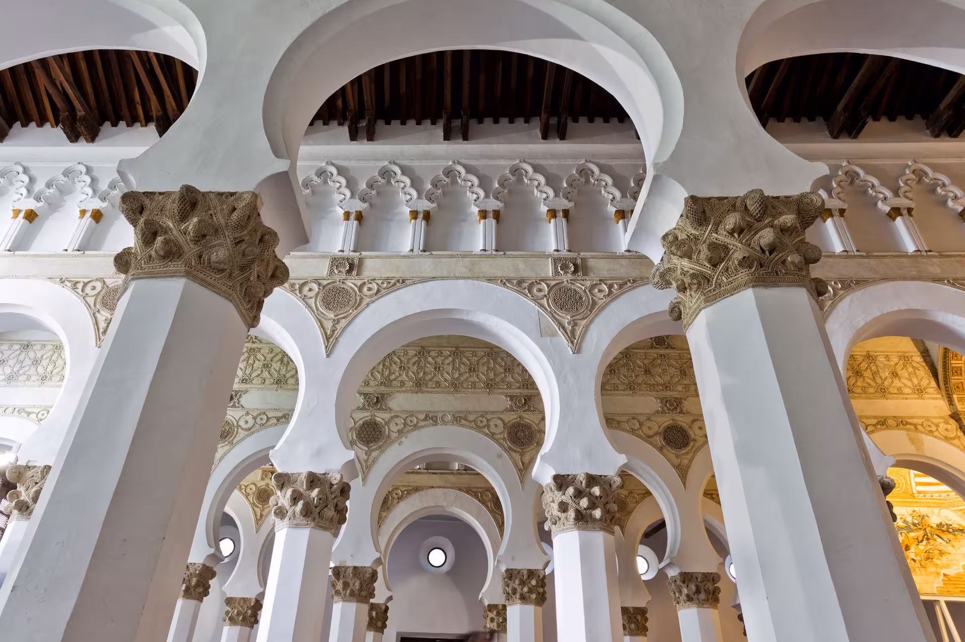 Interior of Toledo's Synagogue of Santa María la Blanca, featuring Moorish arches and detailed craftsmanship.