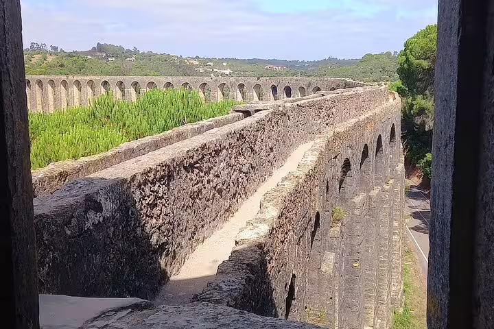 Scenic view of the historic aqueduct in Tomar, Portugal, showcasing its impressive stone arches amidst lush greenery.