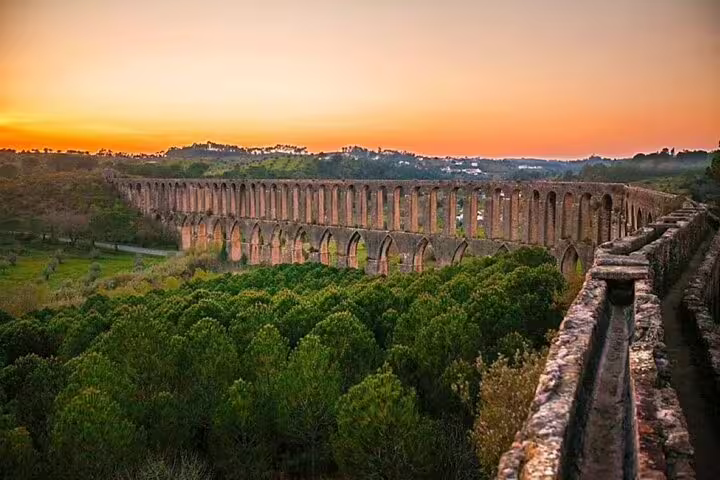 Majestic view of the ancient aqueduct in Tomar at sunset, highlighting lush greenery and historical architecture on a Lisbon day tour.