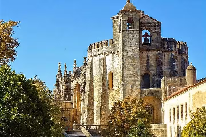 Exterior view of the historic Convent of Christ in Tomar, showcasing its medieval architecture and lush surroundings.