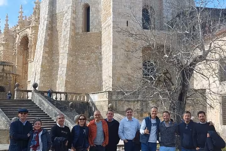 Group of tourists pose outside the historic Convent of Christ, showcasing its stunning architecture in Tomar.