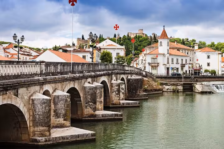 Scenic view of Tomar's ancient bridge and river with the historic castle on the hill, showcasing medieval architecture.