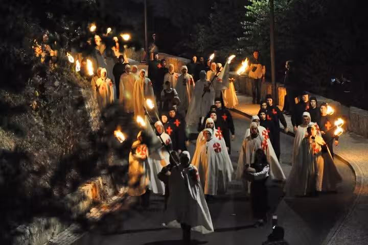Night procession of medieval reenactors with torches in Tomar's historic streets during a private walking tour.