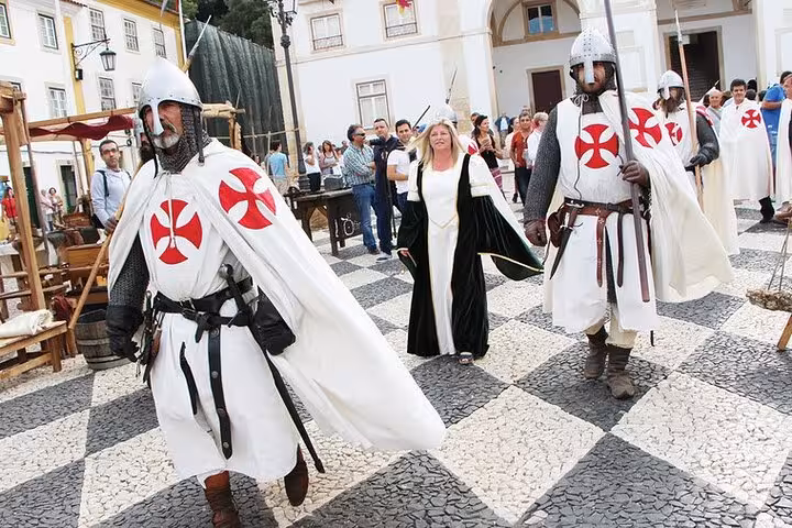 Actors in medieval costumes with Templar symbols parade during a historical reenactment in Tomar's town square.