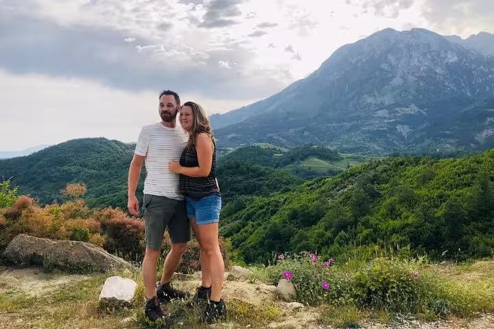 Couple enjoying a breathtaking view of lush green hills and majestic mountains on the Tomor Mountain Lakes of Dardhe hiking tour.