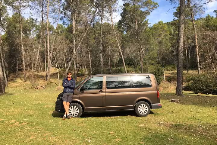 Tour guide stands beside a van in a scenic forest, ready for the Torcal de Antequera hiking tour departure.