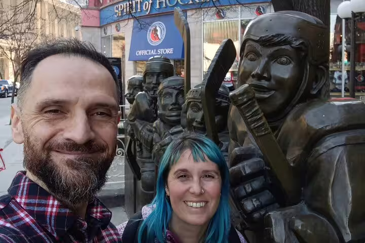 Couple smiling beside bronze hockey player statues outside Spirit of Hockey official store in Toronto