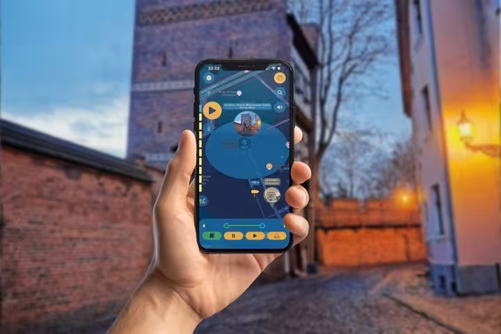Hand holding smartphone with Torun GPS walking tour app displayed on screen in historic old town alley at dusk