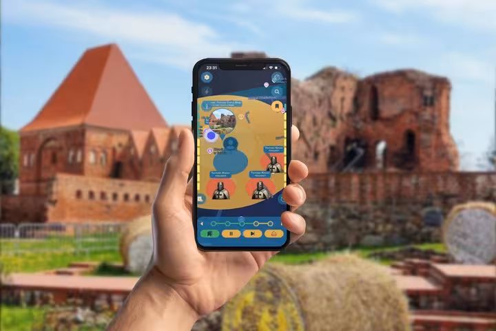 Hand holding smartphone with Copernicus GPS app game map in front of Torun castle ruins