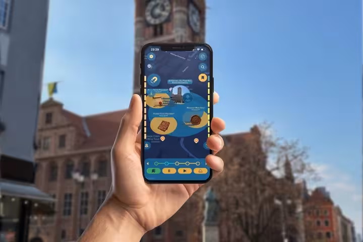 Hand holding smartphone with Copernicus GPS tour app map in front of Torun clock tower